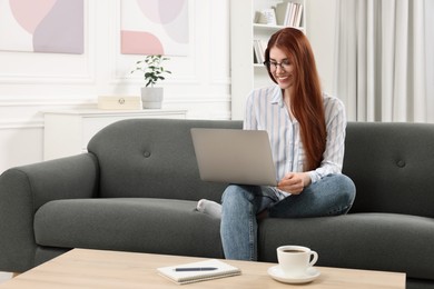 Happy woman using laptop on couch in room