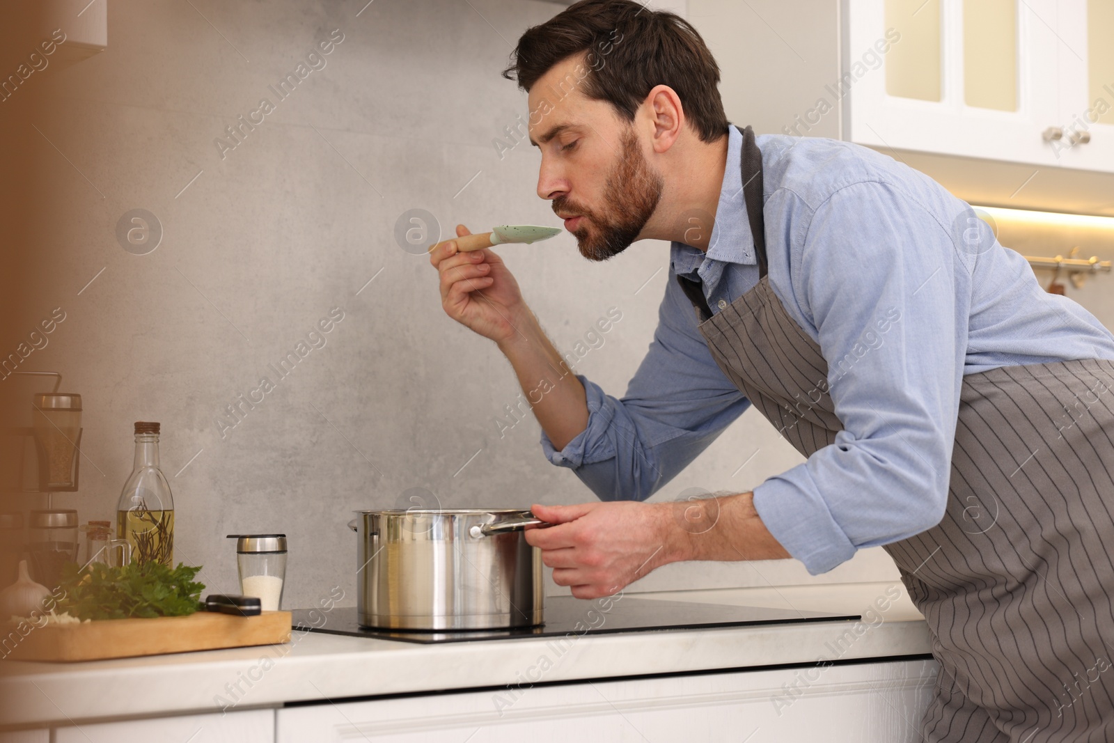 Photo of Man tasting delicious soup with spoon in kitchen