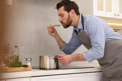 Man tasting delicious soup with spoon in kitchen