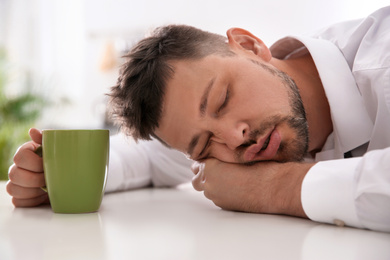 Photo of Man with cup of drink sleeping at home in morning