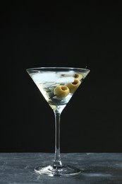 Martini cocktail with ice and olives on grey table against dark background