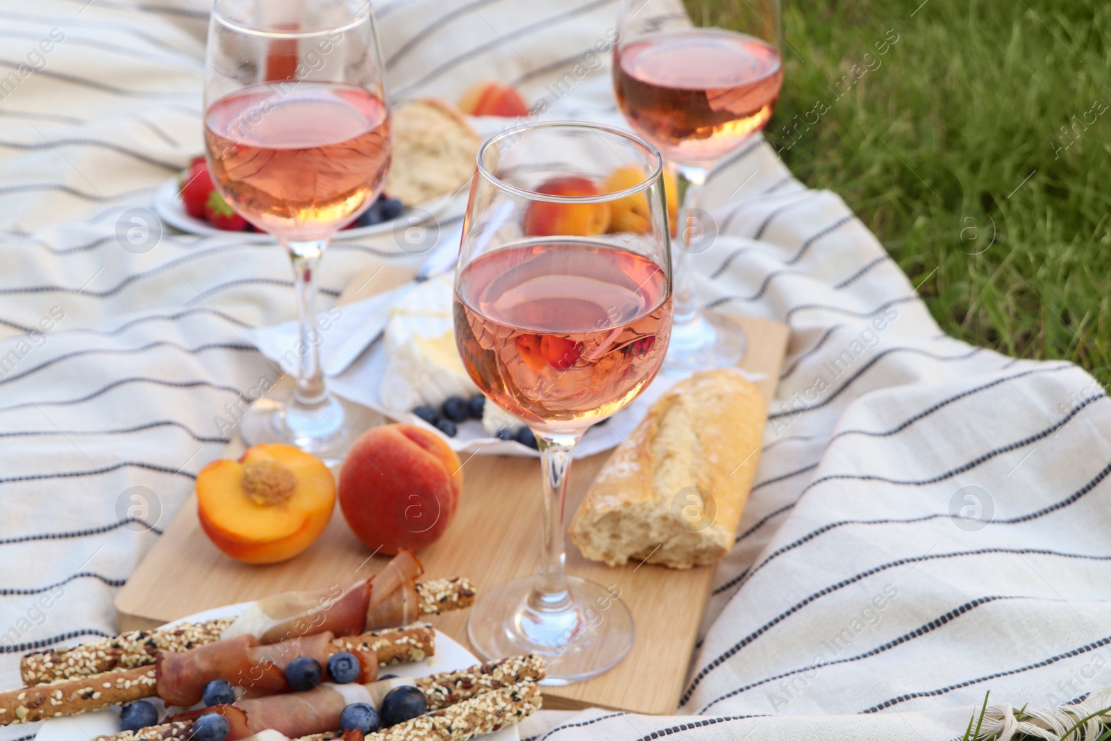 Photo of Glasses of delicious rose wine and food on picnic blanket outdoors