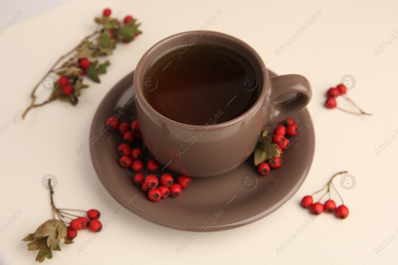 Photo of Brown cup with hawthorn tea and berries on beige table