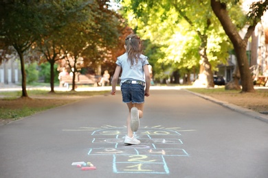 Little child playing hopscotch drawn with colorful chalk on asphalt