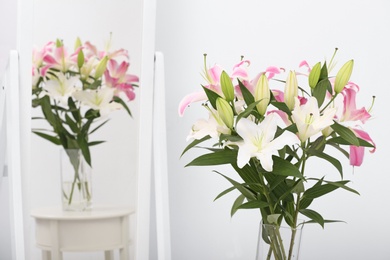 Photo of Vase with bouquet of beautiful lilies on white table near mirror