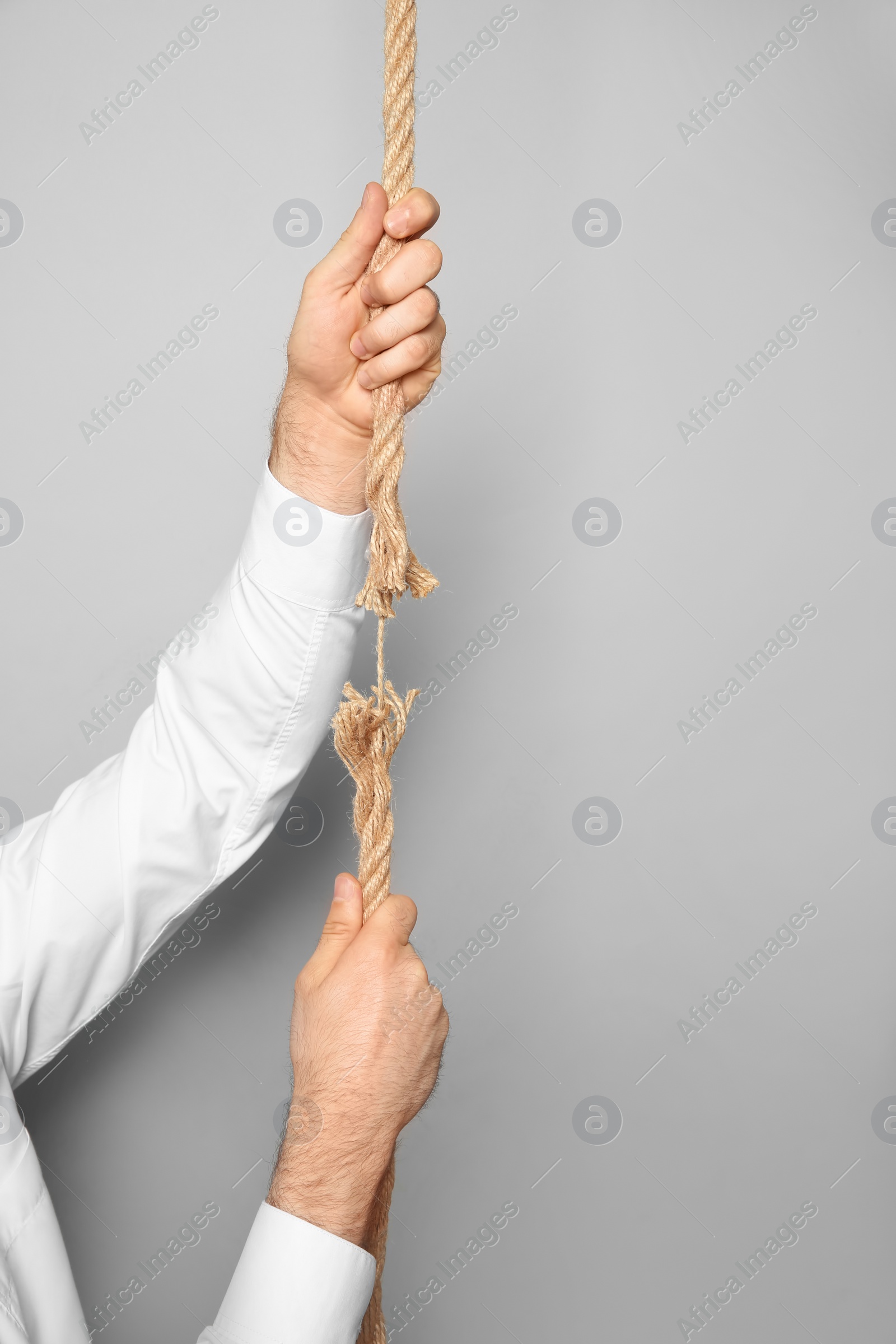Photo of Man climbing frayed rope on gray background
