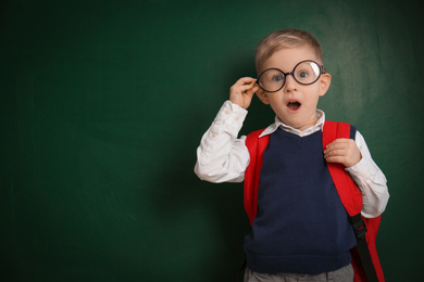 Photo of Funny little child wearing glasses near chalkboard, space for text. First time at school