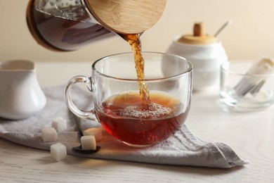 Pouring warm tea into cup on white wooden table, closeup