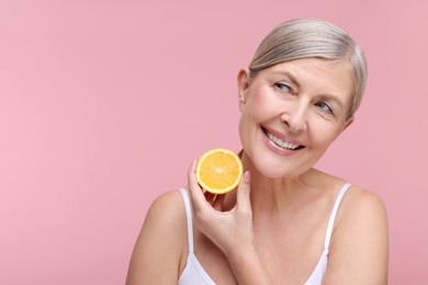 Photo of Beautiful woman with half of orange rich in vitamin C on pink background, space for text