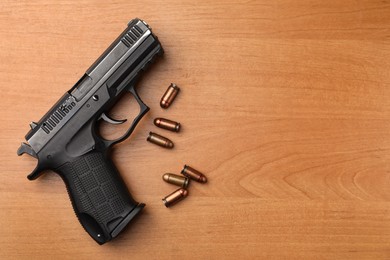 Photo of Semi-automatic pistol and bullets on wooden table, flat lay. Space for text