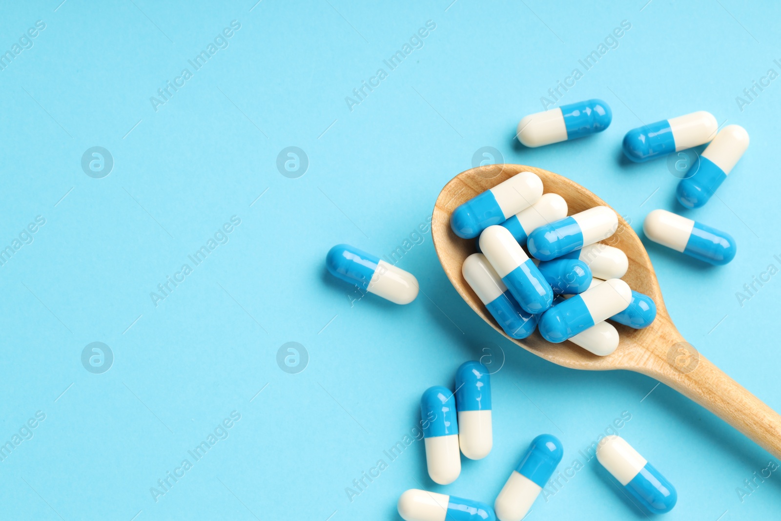 Photo of Many antibiotic pills with wooden spoon and space for text on light blue background, top view. Medicinal treatment