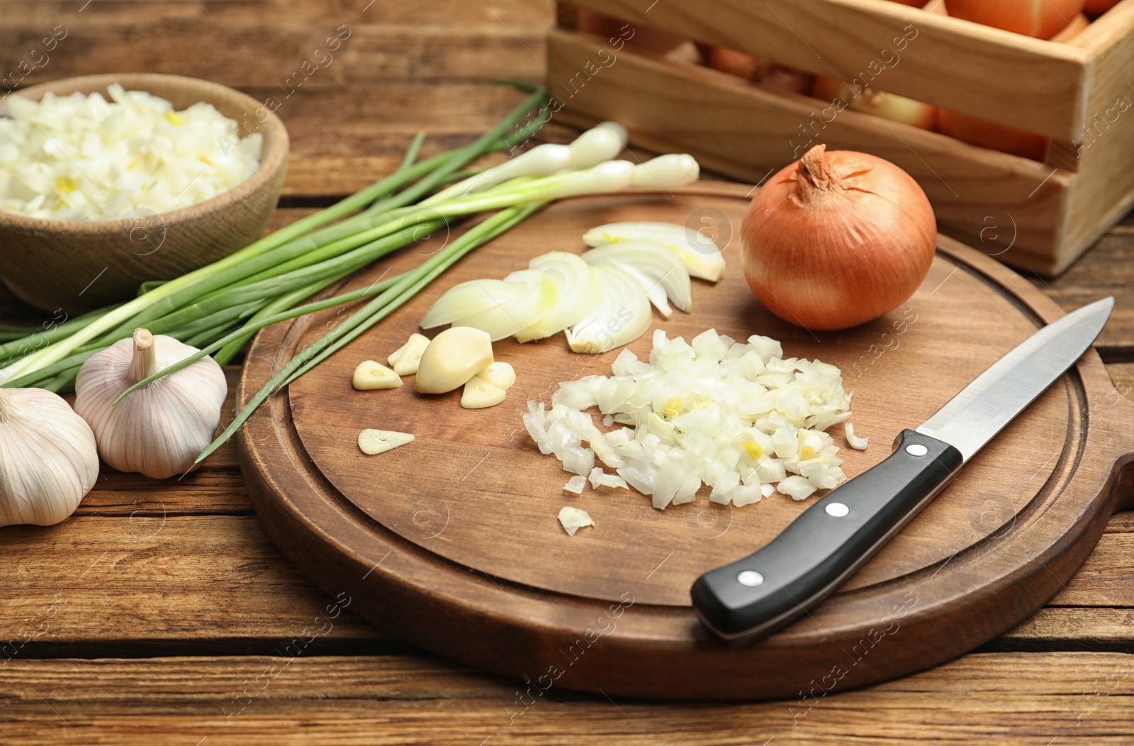 Photo of Board with cut onion and garlic on wooden table