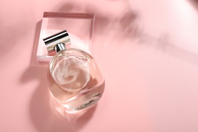 Bottle of luxury women's perfume in sunlight on pink background, above view. Space for text