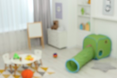 Photo of Blurred view of child`s playroom with different toys and furniture. Stylish kindergarten interior