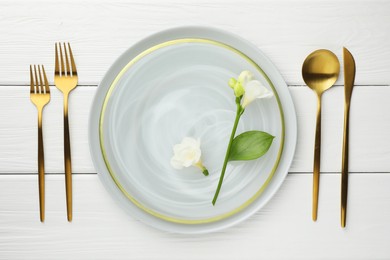 Stylish setting with cutlery, flowers and plate on white wooden table, flat lay