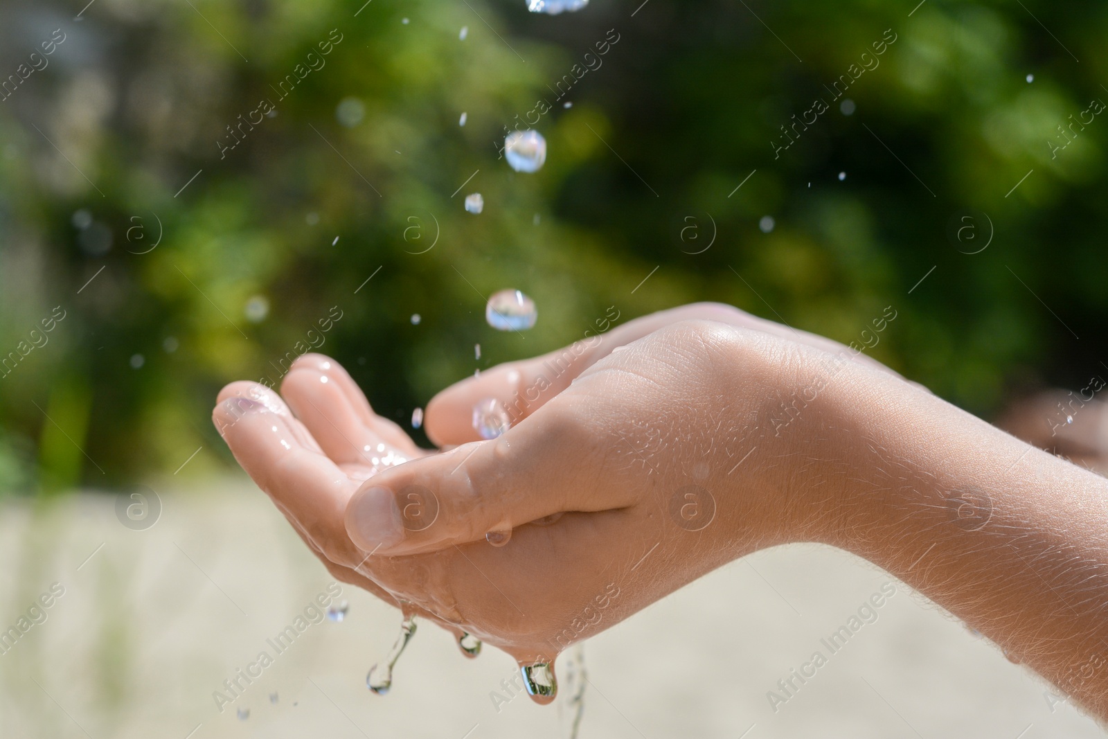 Photo of Pouring water into kid`s hand outdoors, closeup