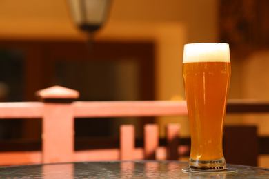 Photo of Glass of tasty beer on table outdoors, space for text