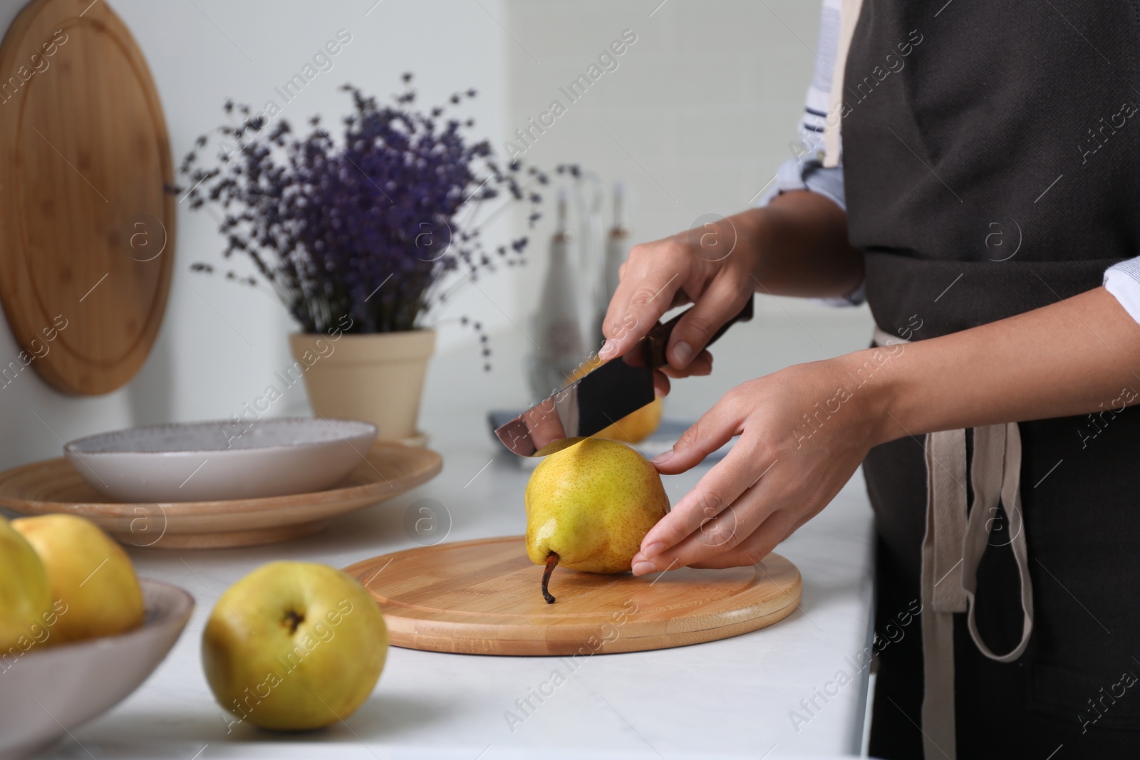 Photo of Woman cutting fresh ripe pear at table in kitchen, closeup