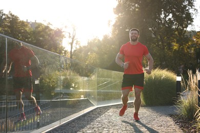 Photo of Happy man running outdoors on sunny day. Space for text
