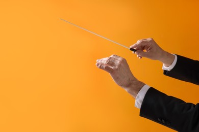 Photo of Professional conductor with baton on orange background, closeup. Space for text