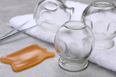 Photo of Glass cups, towel and gua sha on grey table, closeup. Cupping therapy