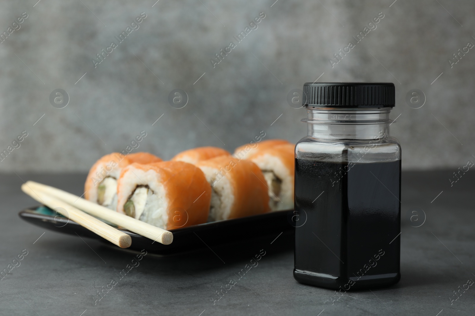 Photo of Bottle of tasty soy sauce, chopsticks and sushi rolls with salmon on grey table