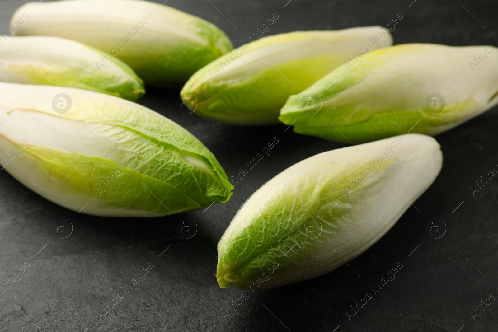 Photo of Fresh raw Belgian endives (chicory) on black table, closeup