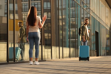 Photo of Long-distance relationship. Woman waving to her boyfriend with luggage near building outdoors