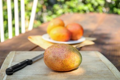 Photo of Tasty mango and knife on wooden board outdoors