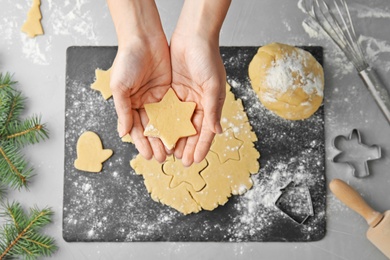 Photo of Young woman holding raw Christmas cookie over table, top view