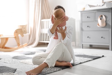 Photo of Young mother with her little baby sitting on floor at home