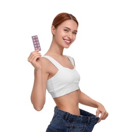 Slim woman in big jeans with pills on white background. Weight loss