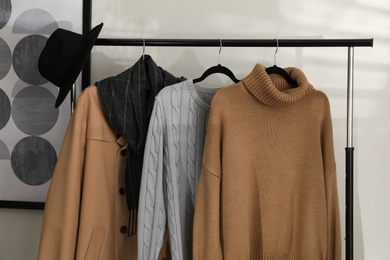 Different stylish warm clothes on rack indoors
