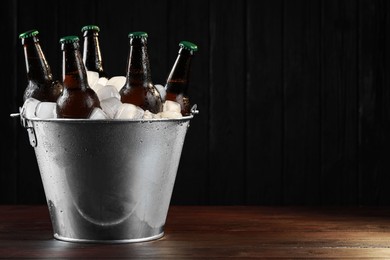 Metal bucket with bottles of beer and ice cubes on wooden table, space for text