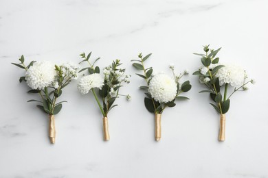 Small stylish boutonnieres on white marble table, flat lay