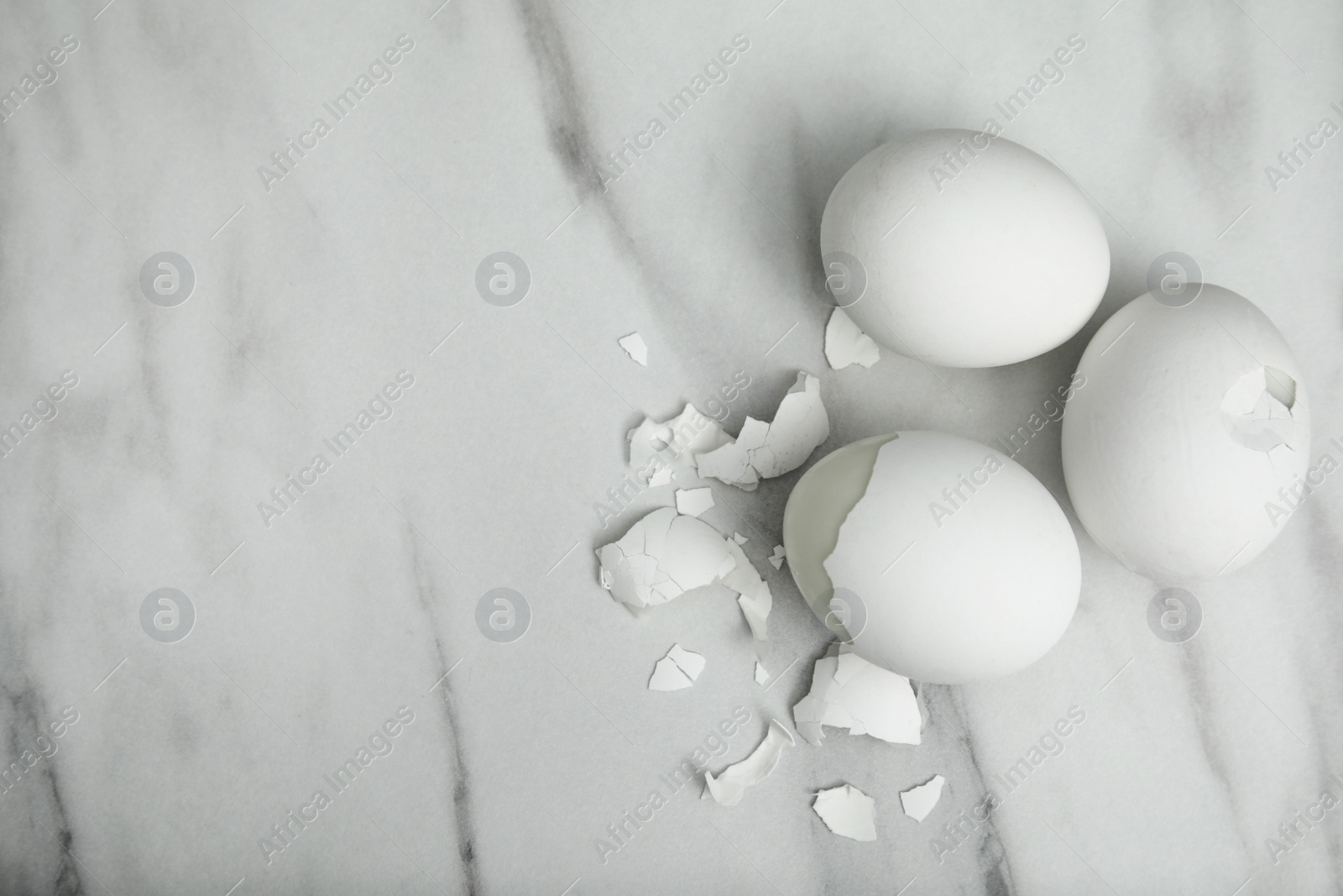 Photo of Boiled chicken eggs and pieces of shell on white marble table, flat lay. Space for text