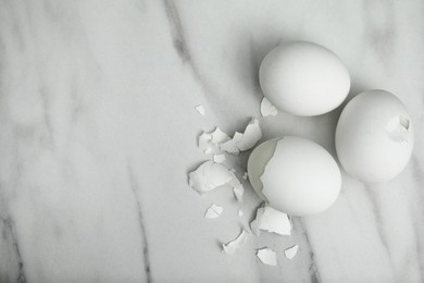 Boiled chicken eggs and pieces of shell on white marble table, flat lay. Space for text