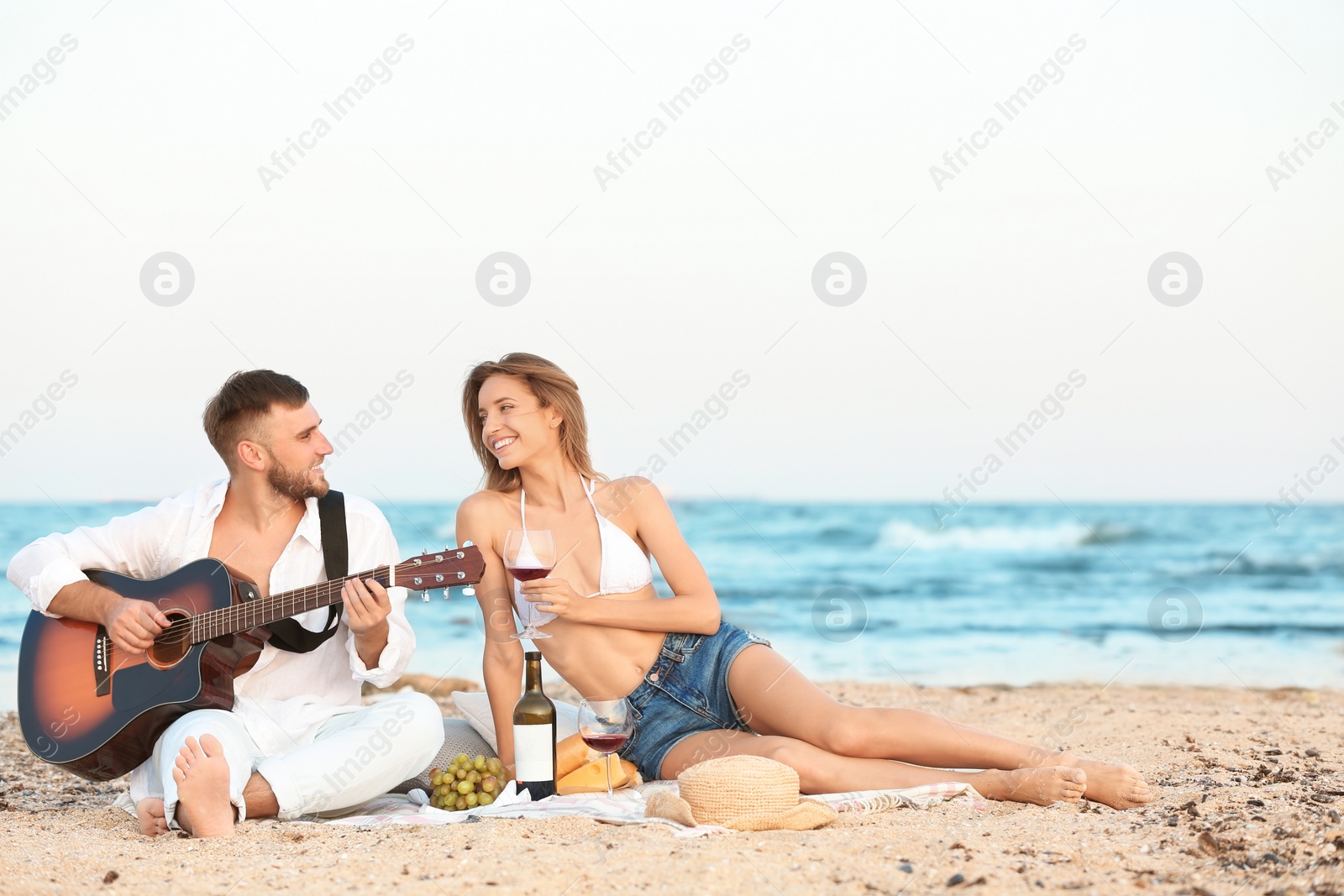 Photo of Young couple with guitar having romantic dinner on beach