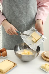 Photo of Woman adding fresh butter into bowl with flour at white table, closeup