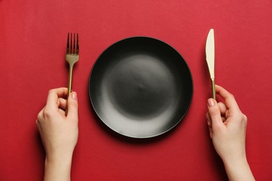 Photo of Woman with empty plate and cutlery on red background, top view