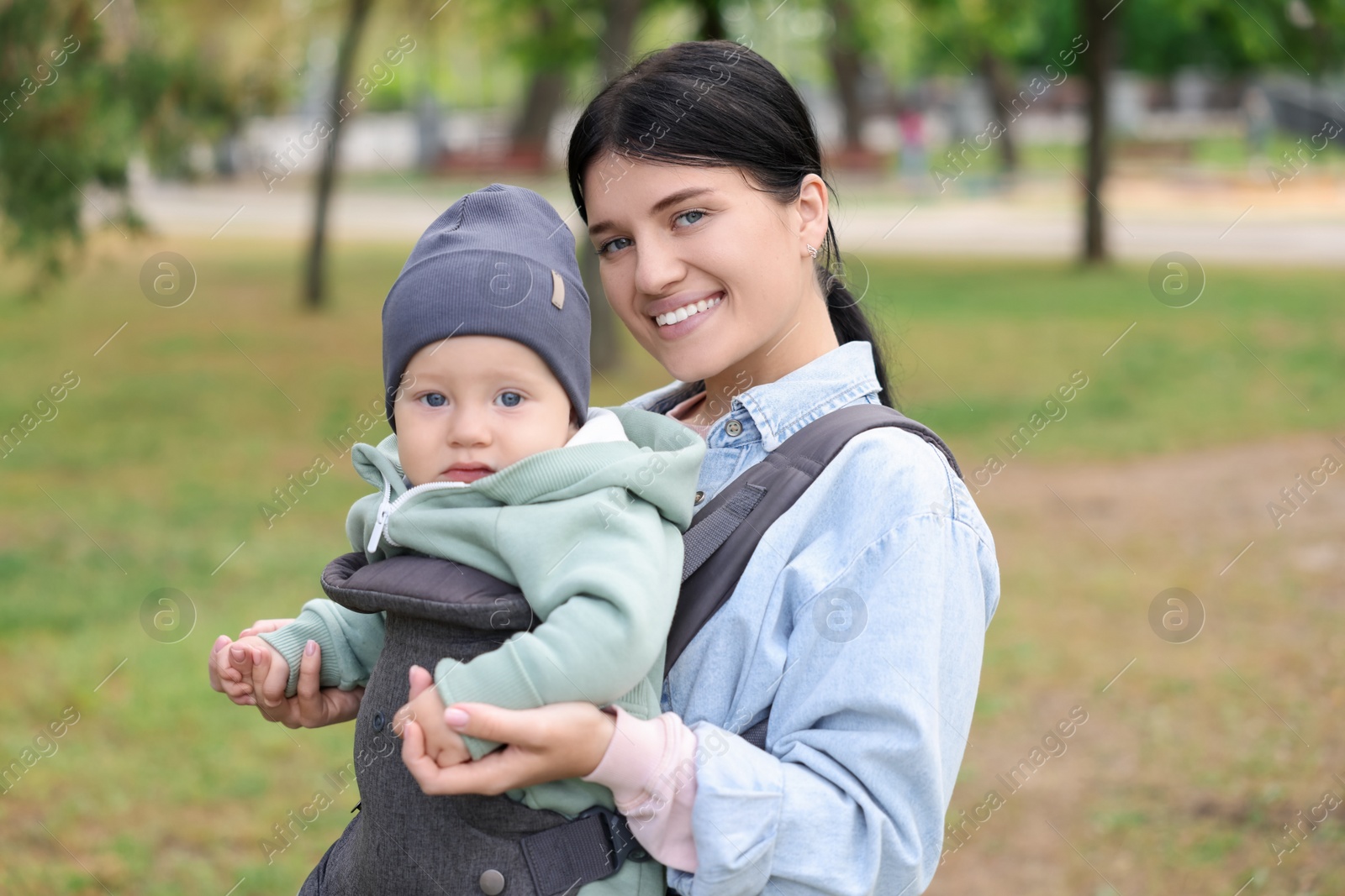 Photo of Mother holding her child in sling (baby carrier) in park