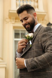 Photo of Young groom wearing engagement ring with beautiful boutonniere outdoors. Preparing for wedding