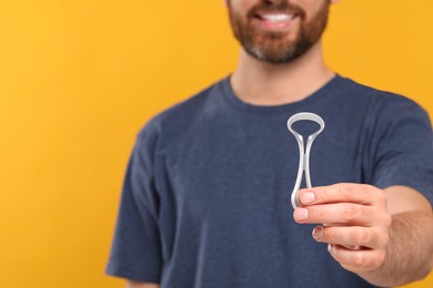 Man with tongue cleaner on yellow background, closeup. Space for text