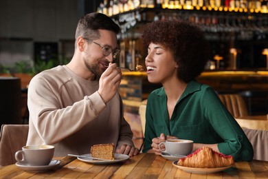 Photo of International dating. Handsome man feeding his girlfriend with cake in cafe
