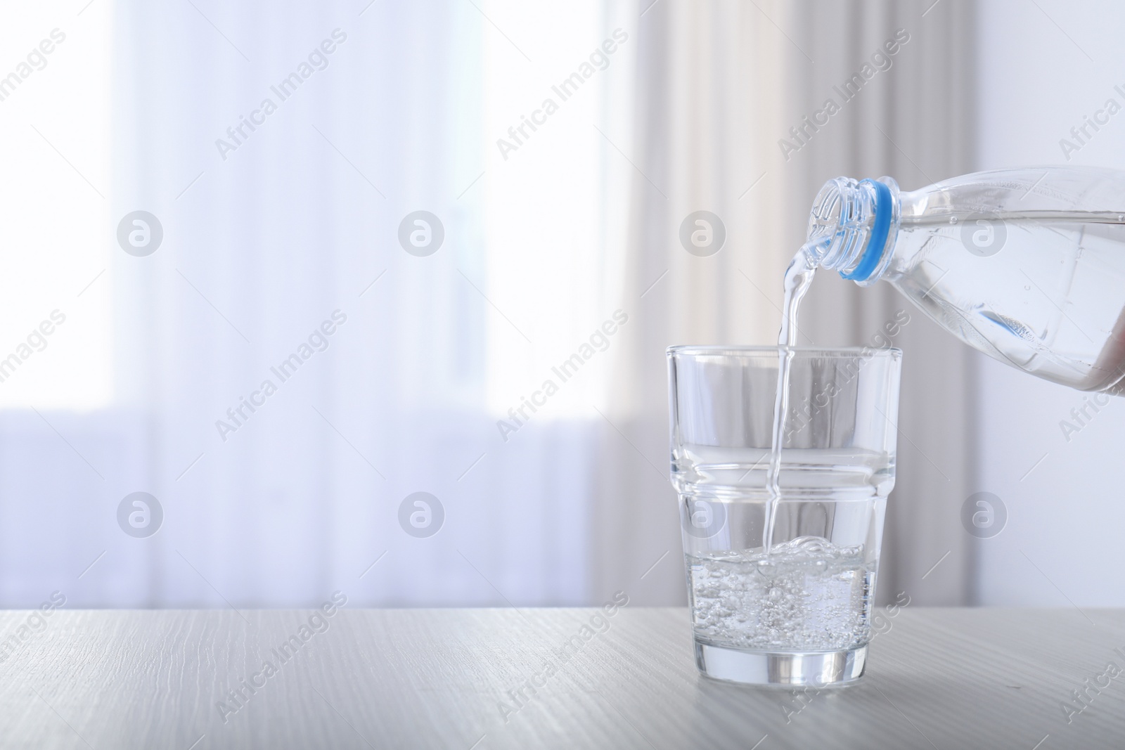 Photo of Pouring water from bottle into glass on blurred background. Space for text