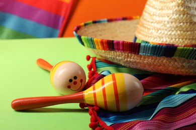 Mexican sombrero hat, poncho and maracas on green table, closeup