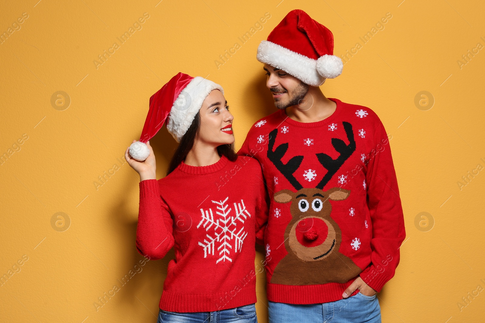 Photo of Young couple in Christmas sweaters and hats on color background