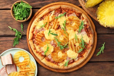 Delicious pineapple pizza and ingredients on wooden table, flat lay