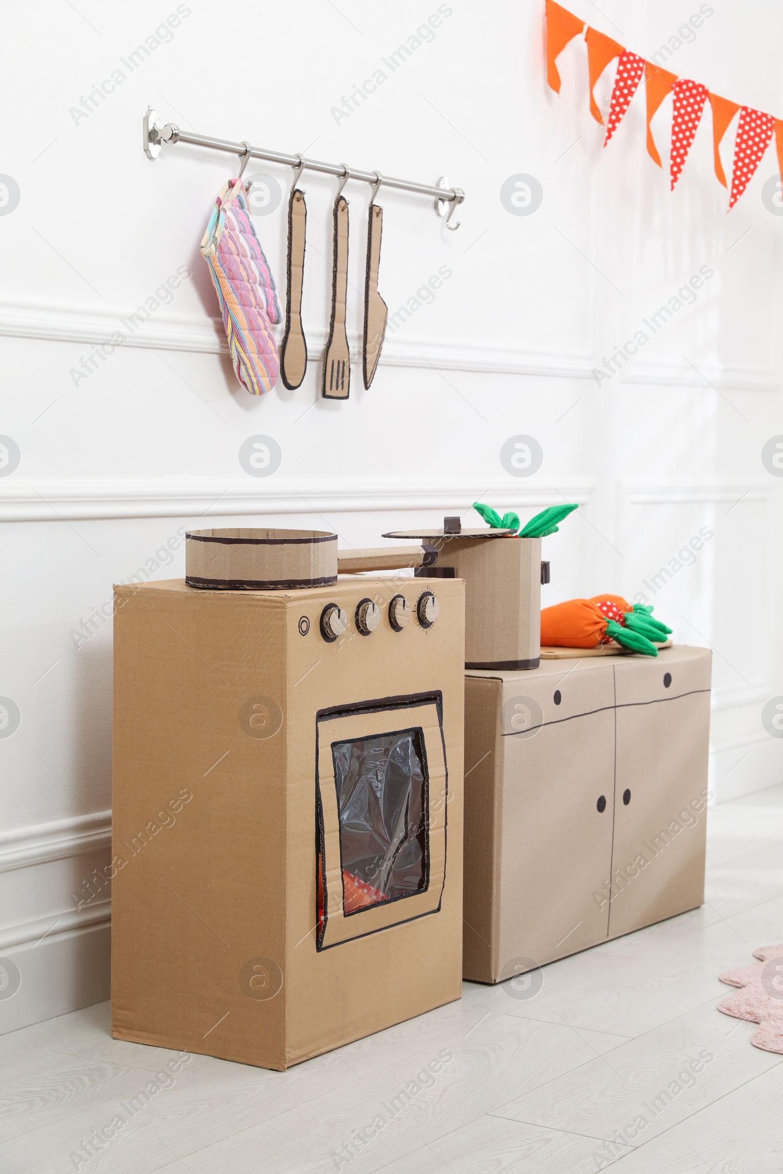 Photo of Toy cardboard kitchen with stove and utensils indoors