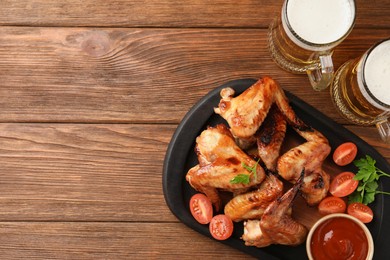 Mugs with beer, delicious baked chicken wings and sauce on wooden table, flat lay. Space for text